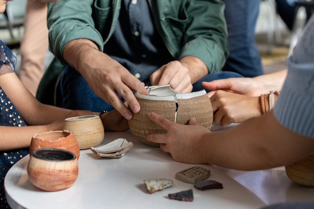 Manos de varias personas uniendo una vasija de cerámica